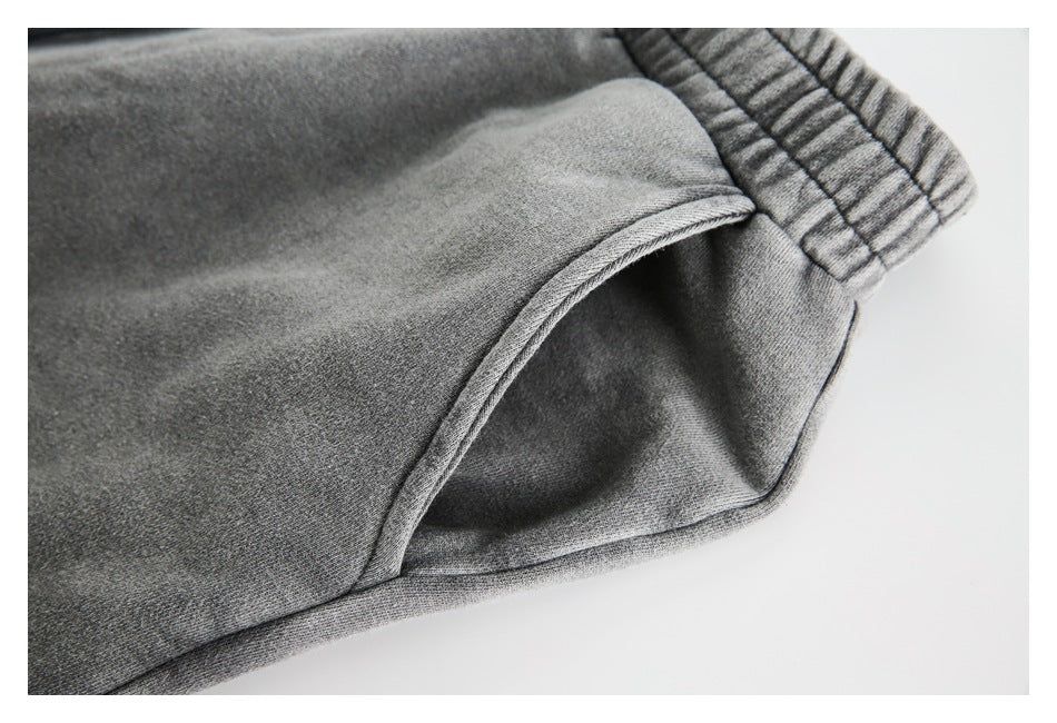 Close-up of a curved side pocket and stitching on gray sweatpants.