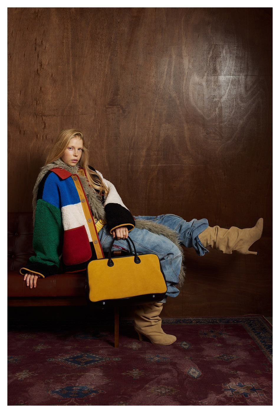 Model seated in a multicolor fleece jacket with contrasting panels, red collar and large patch pockets.