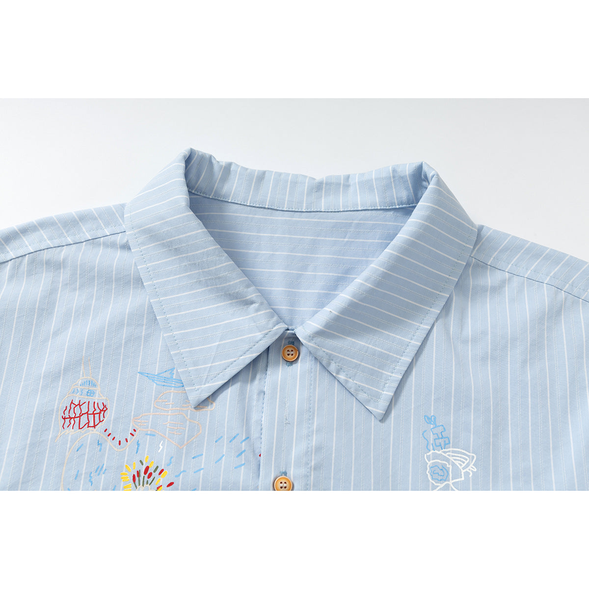 Close-up of a light blue pinstriped shirt collar, buttons, and colorful illustrated front embroidery.