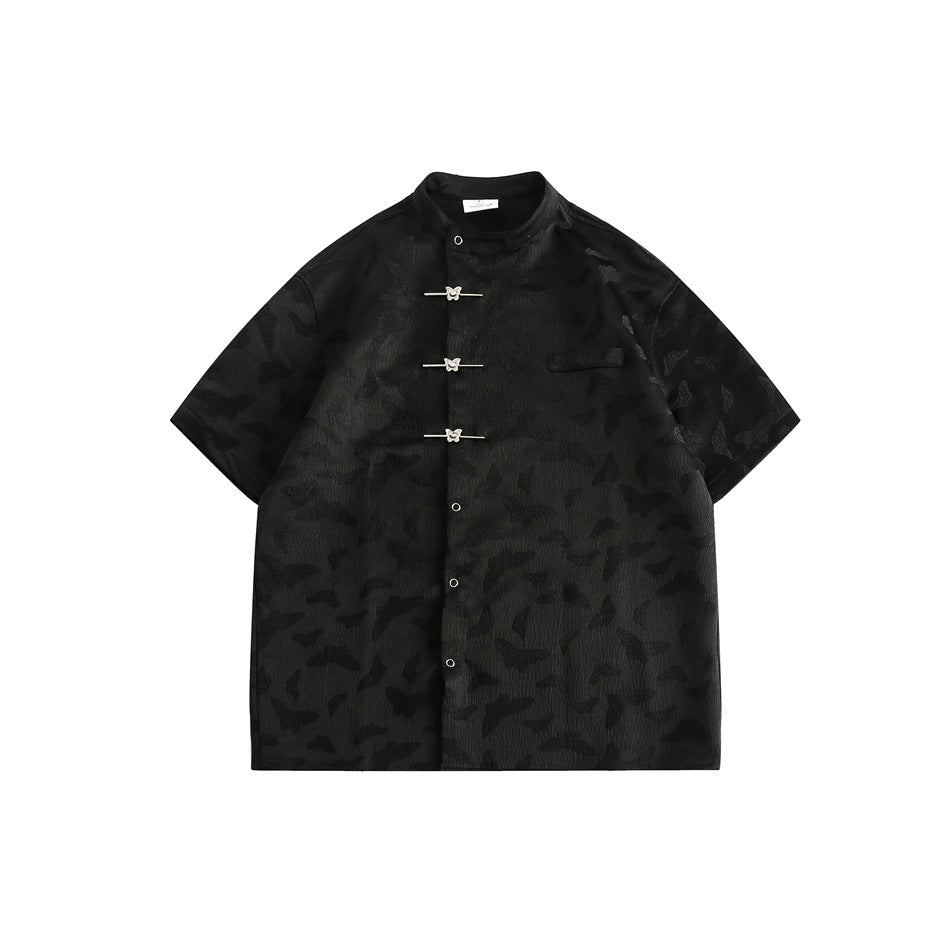 Black short-sleeve stand-collar shirt with tonal butterfly pattern, metal toggle closures, snaps and chest pocket, flat lay