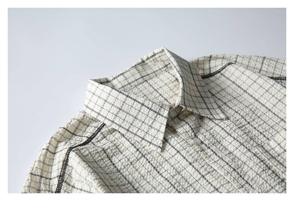 Framed close-up of the pointed collar and shoulder seam on a cream shirt with a black windowpane check.