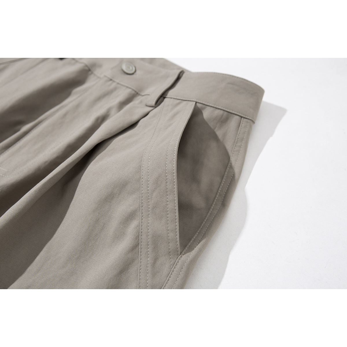 Angled close-up of taupe cargo pants showing the waistband and stitched front pocket opening.