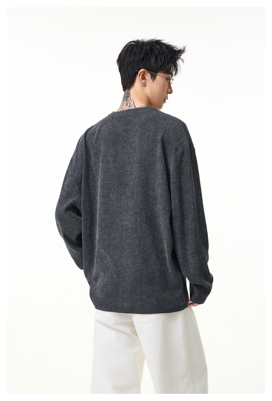Back view of a model wearing a charcoal gray textured long-sleeve top with white trousers.