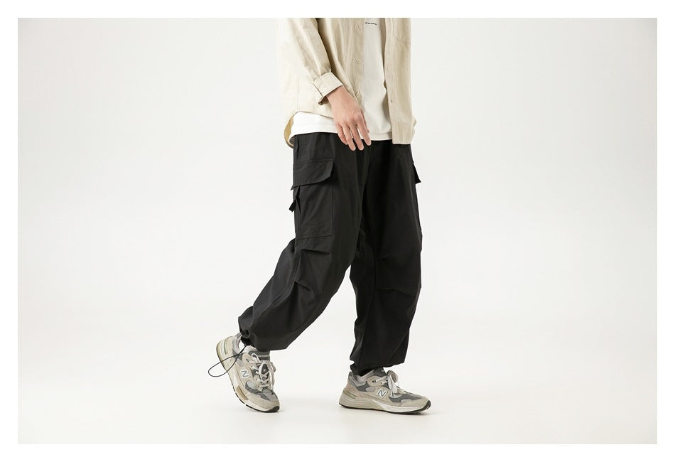 Model wearing loose black cargo pants with large flap pockets, shown in a walking pose from a front angle.