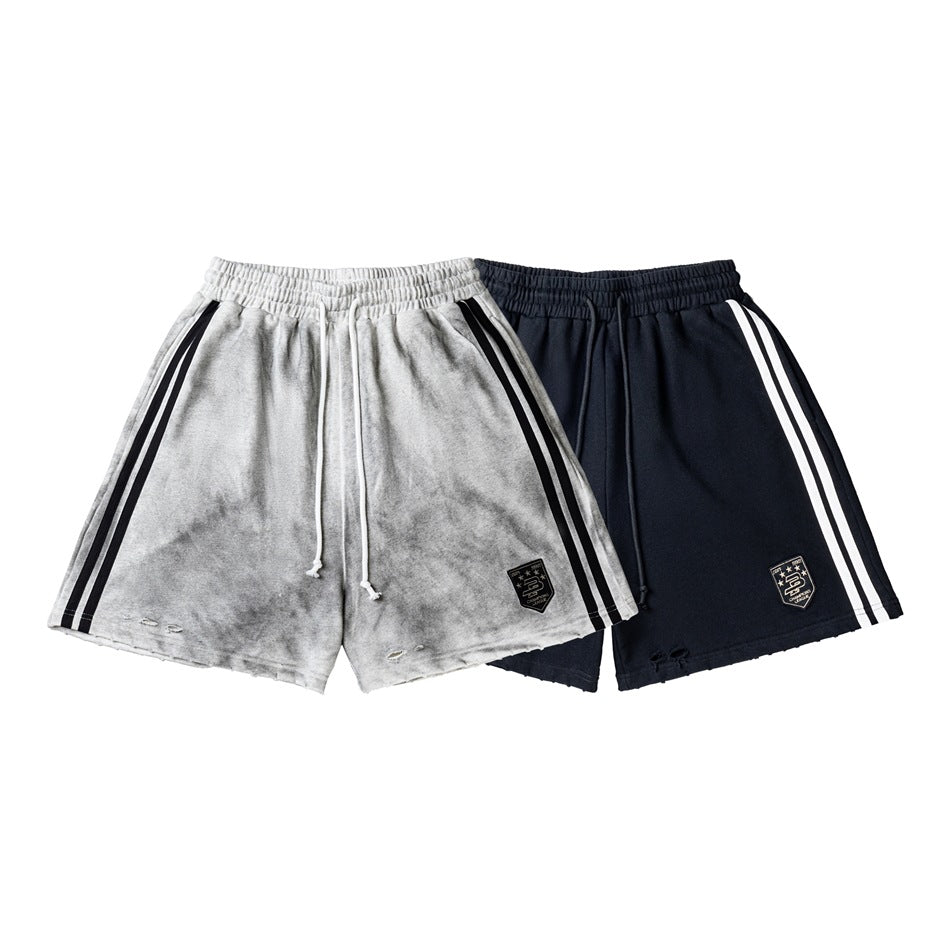 Front view of gray and black athletic shorts with elastic drawstring waists, twin side stripes, shield patches, and