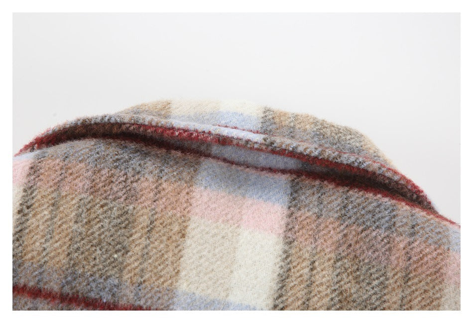 Close-up of a folded beige, gray, pale pink, and blue plaid garment with red stripes.
