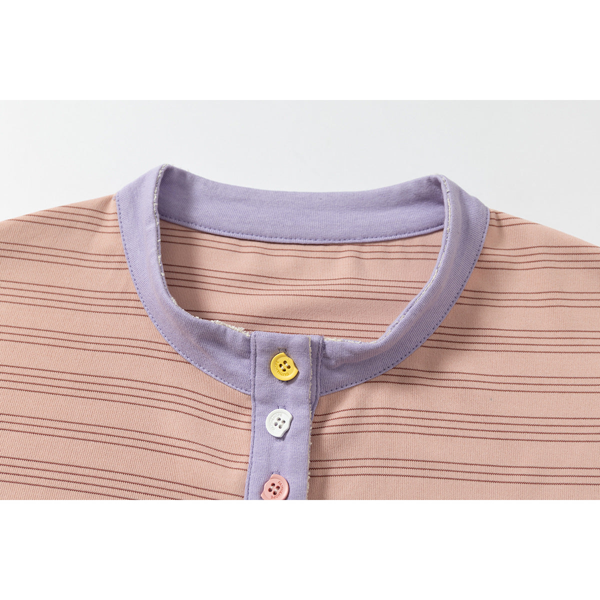 Close-up of a peach-pink finely striped shirt with a lavender collar and placket and assorted colorful buttons.