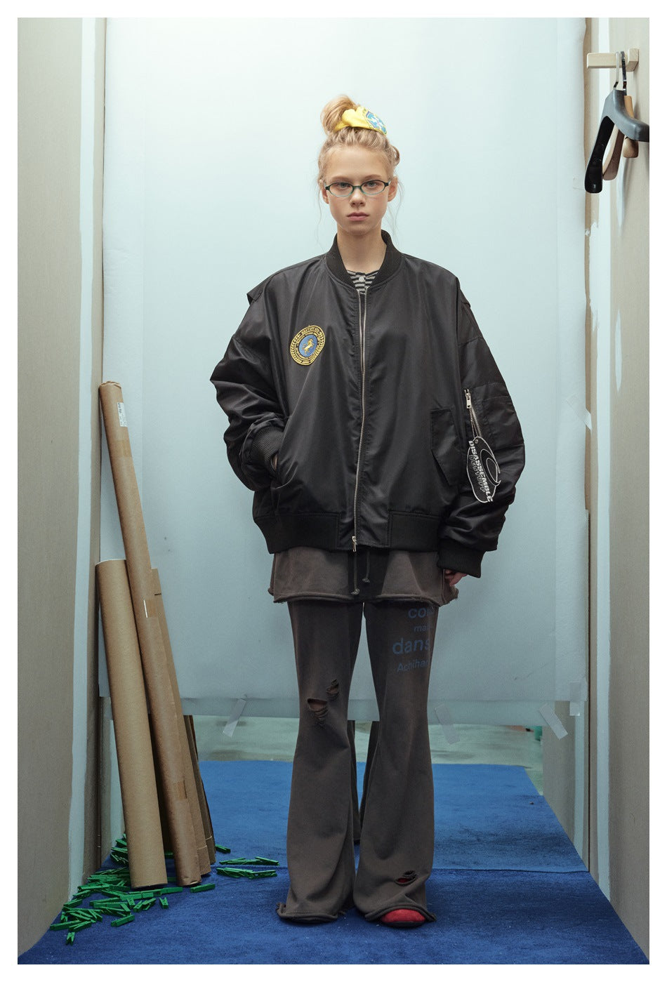 Front view of a model in an oversized black bomber jacket with a chest patch and zippered sleeve pocket.