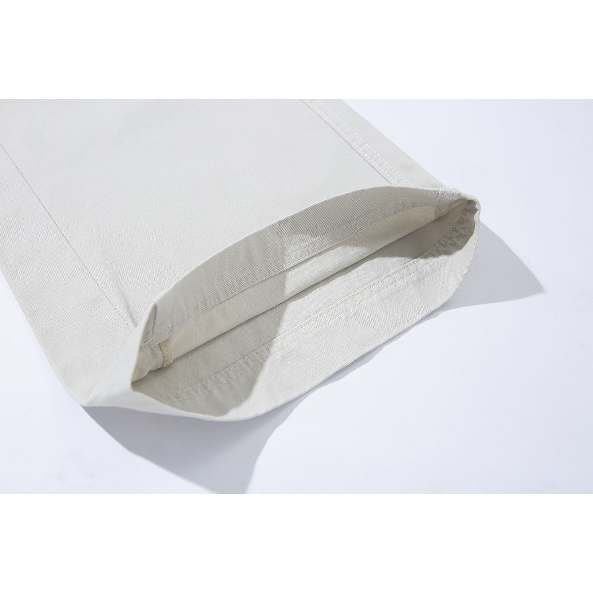 Close-up of the cuff and double-stitched hem of ivory trousers.