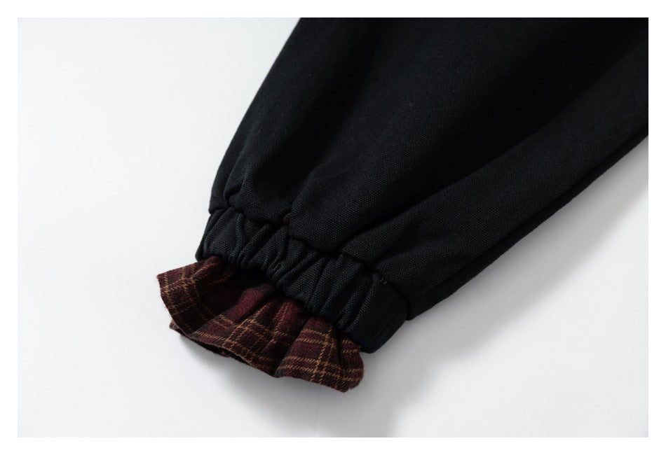 Close-up of a gathered black cuff with burgundy plaid fabric showing at the edge.