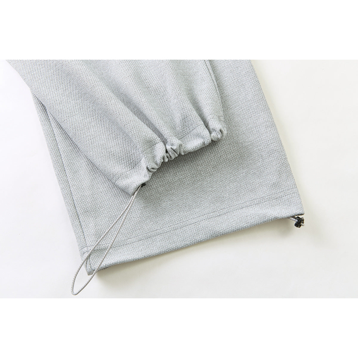 Close-up of the gathered ankle cuff and adjustable cord at the hem of light gray pants.