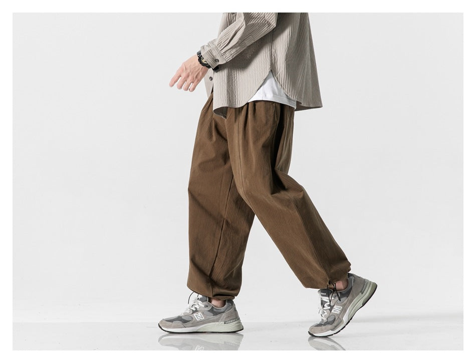 Model walking in loose brown trousers with adjustable drawcord hems.