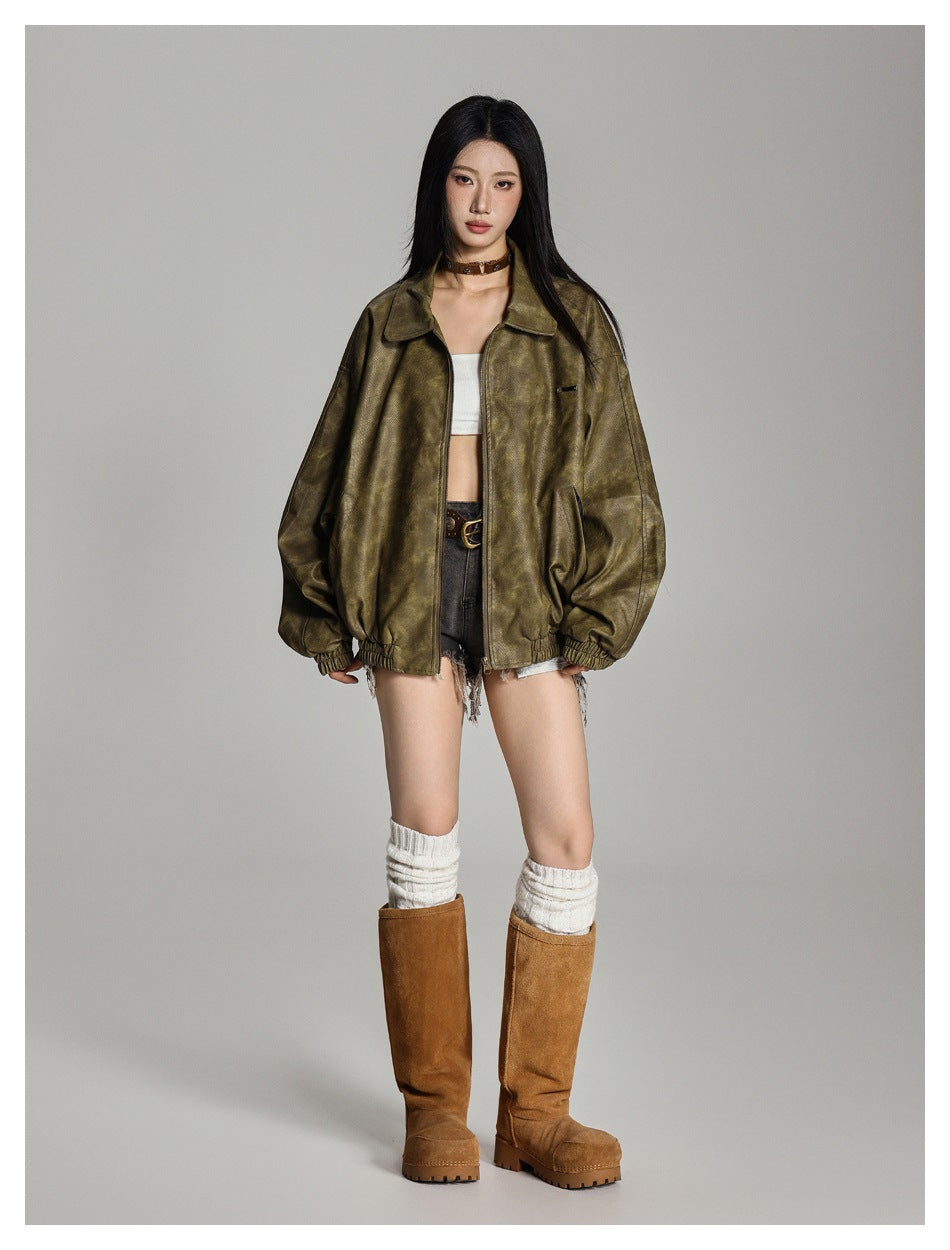 Model wearing an olive green oversized zip jacket open over a white top, denim shorts and tall tan boots