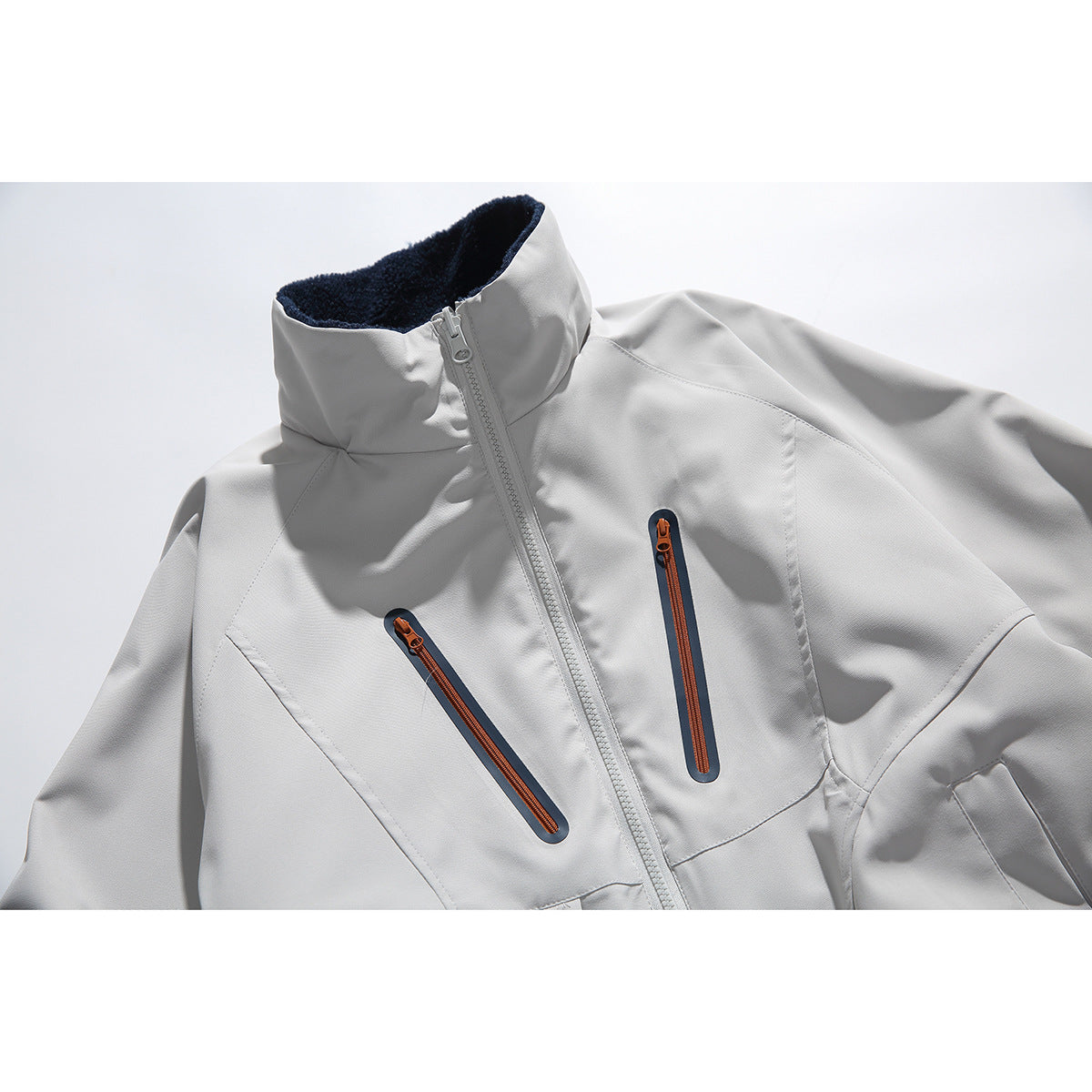 Close-up of a light gray jacket with a high fleece-lined collar, center zipper, and two orange-accented chest zippers.