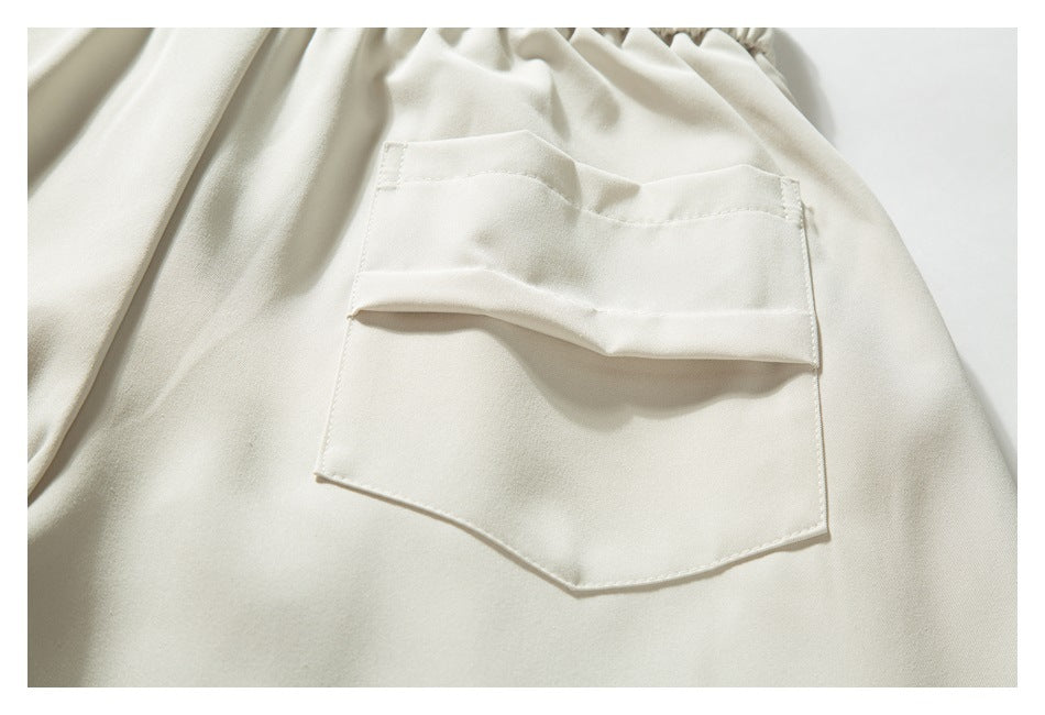 Close-up of an ivory trouser pocket with a folded flap and angular lower edge.