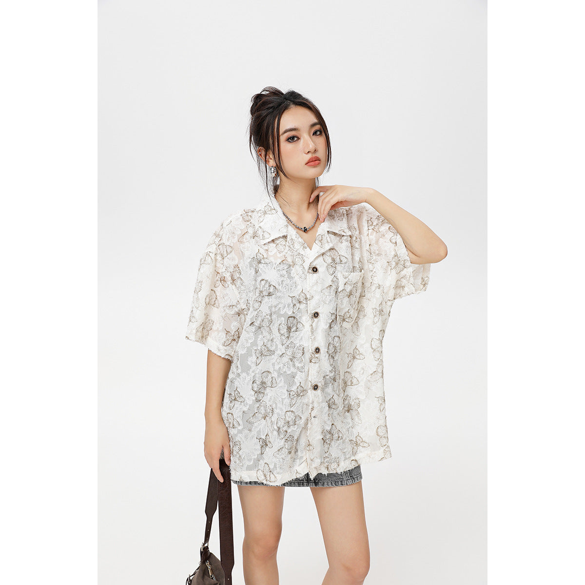 Model wearing a loose ivory short-sleeve button-up shirt with a muted beige-gray floral and butterfly pattern.