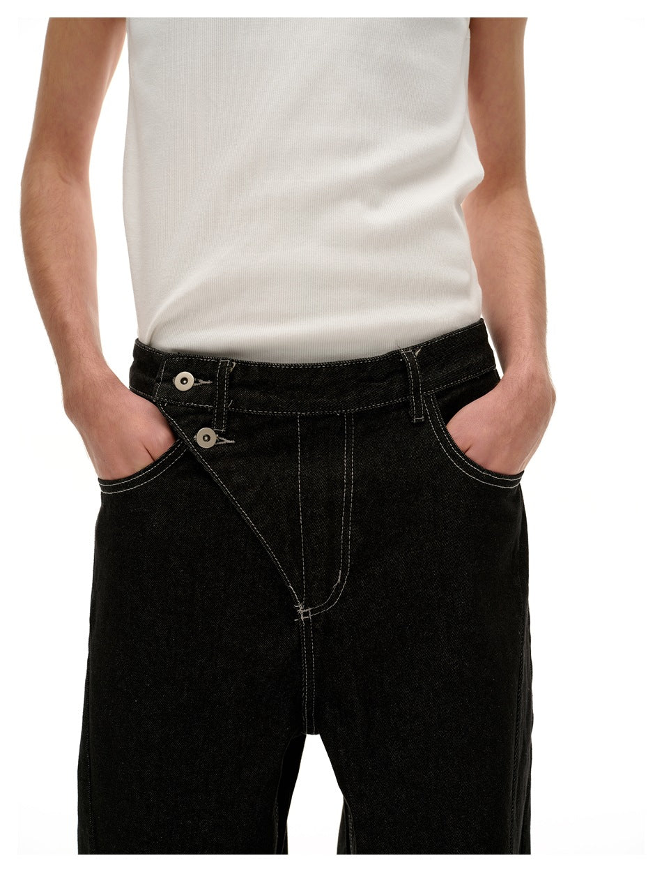 Close-up of black jeans showing the waistband, two-button fly, front pockets, and contrast stitching.