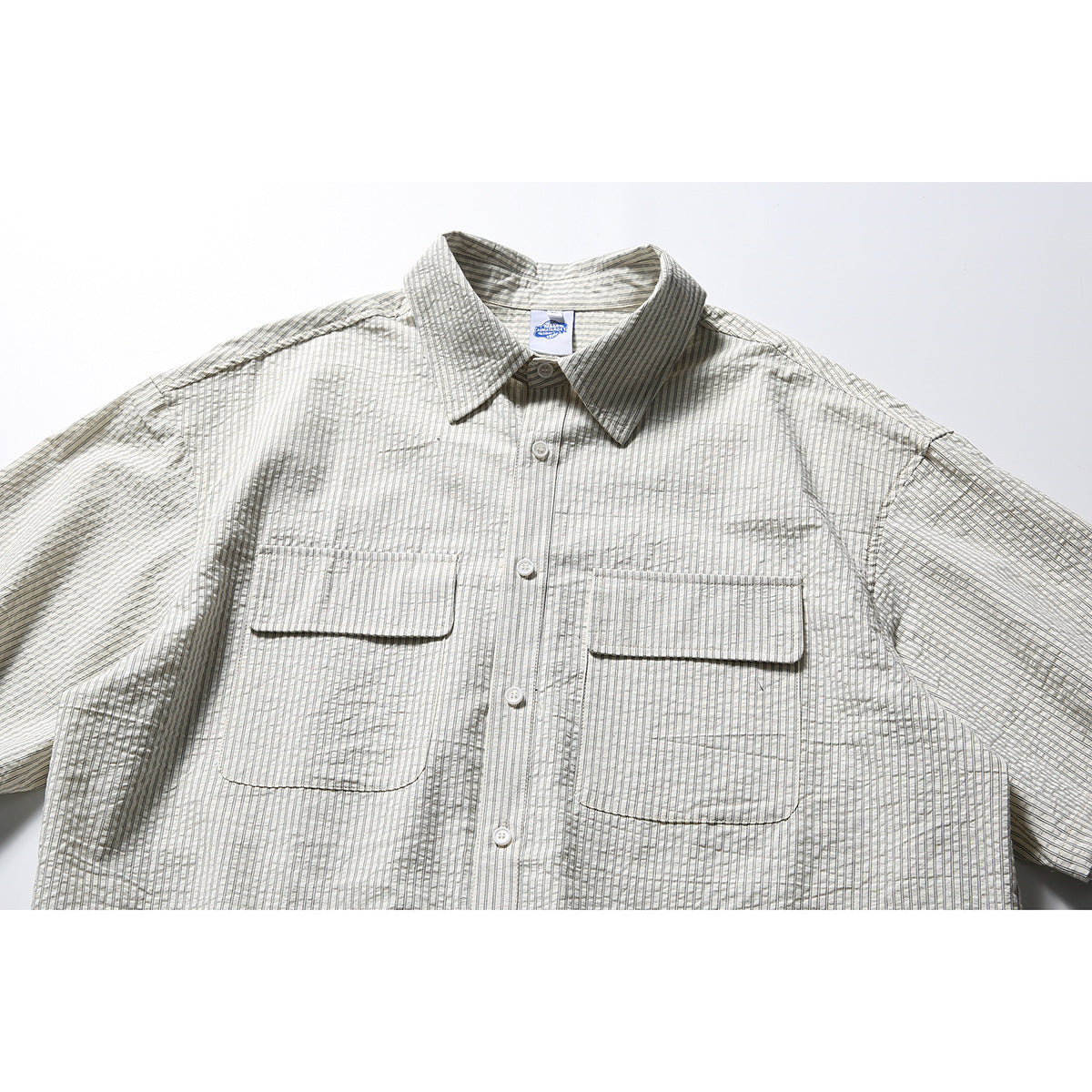 Close-up of a light gray short-sleeve button-up shirt with fine dark stripes and two flap chest pockets.