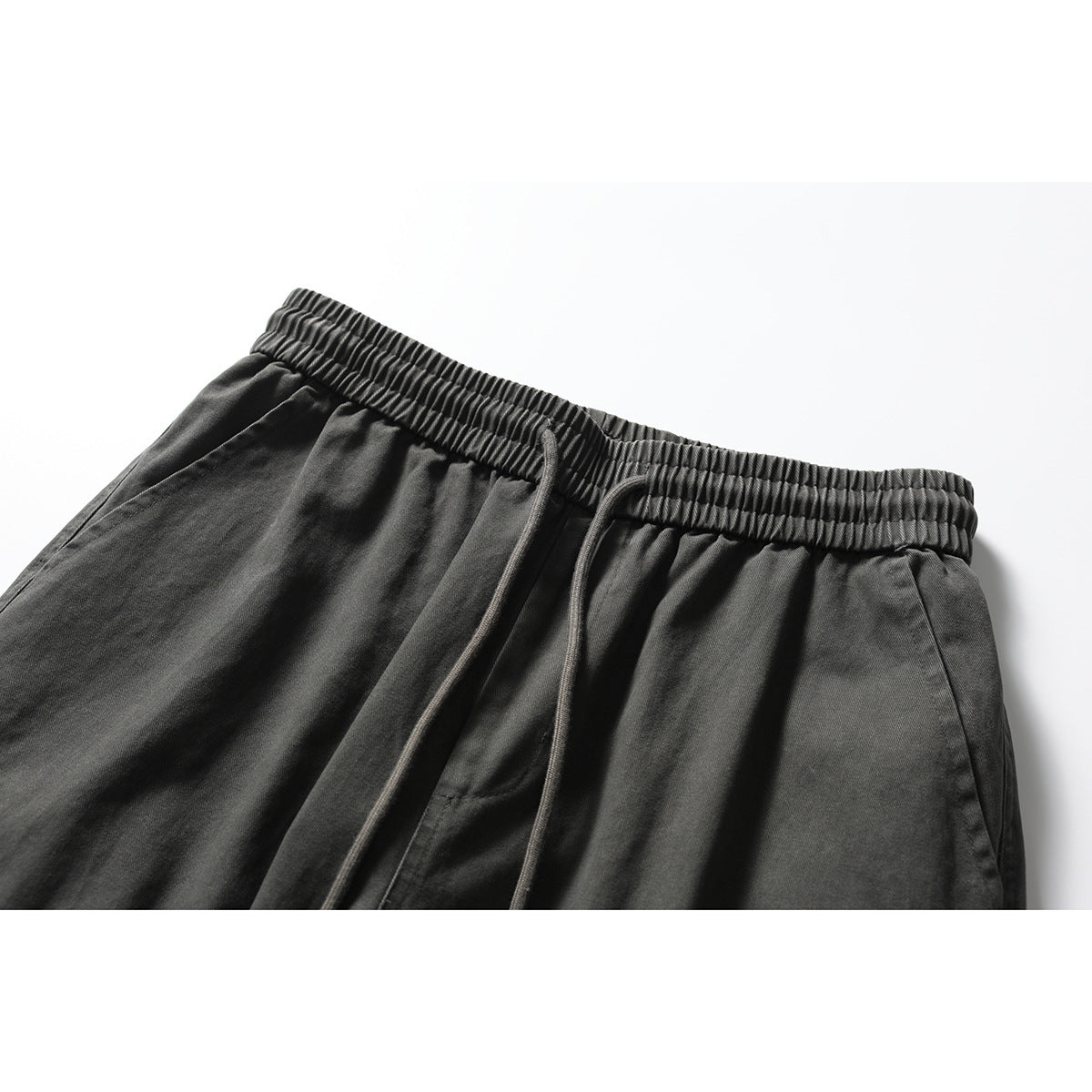Close-up of charcoal pants showing the gathered elastic waistband, drawstrings, and angled front pocket.