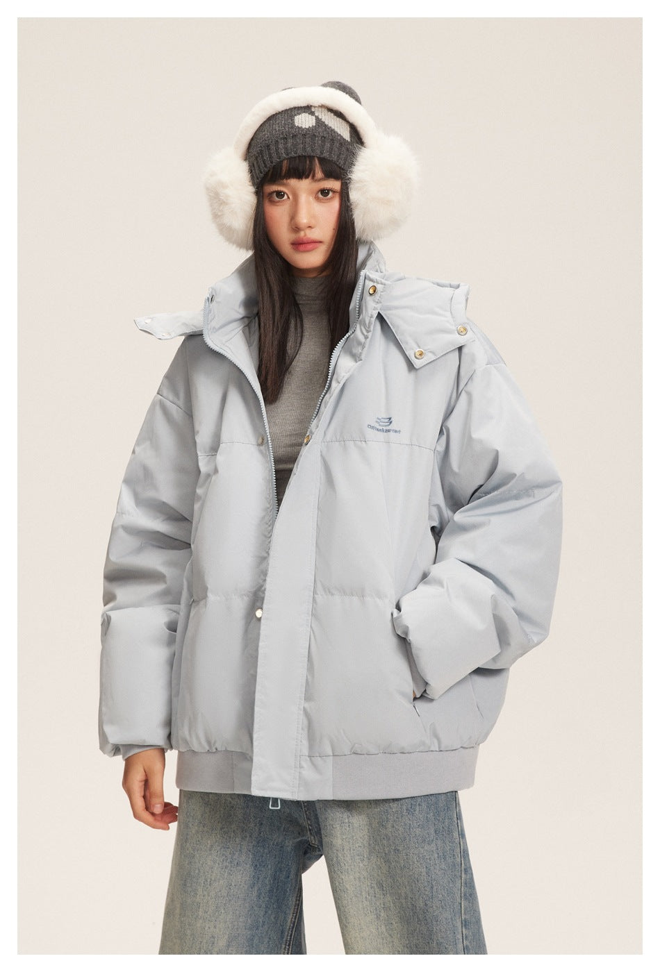 Front view of a model wearing a light gray hooded puffer jacket with snap closures and a zip front.