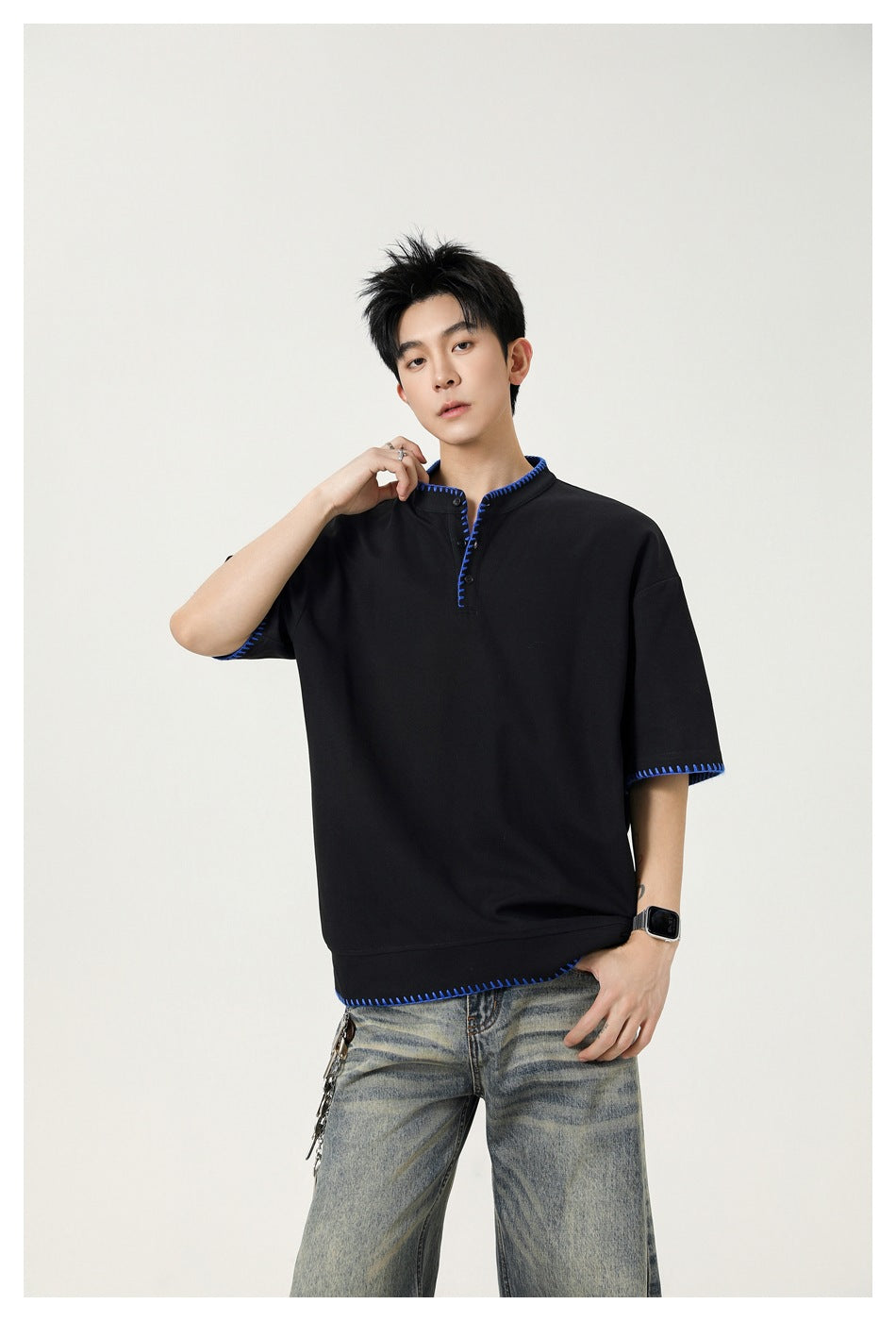 Model wearing a black short-sleeve henley with bright blue contrast stitching and light-wash jeans.