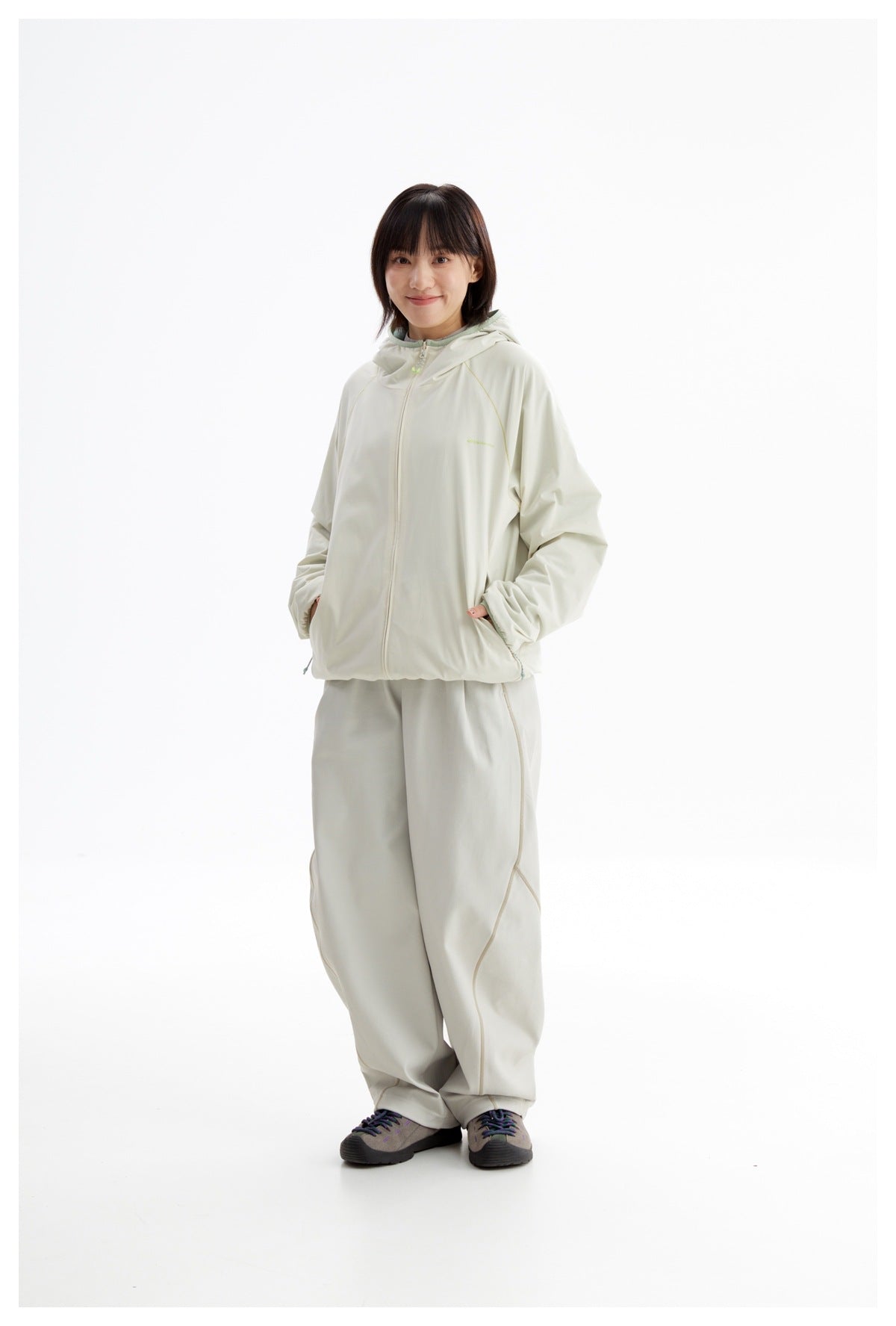 Model wearing a pale ivory hooded zip jacket and matching loose pants with curved seam details.
