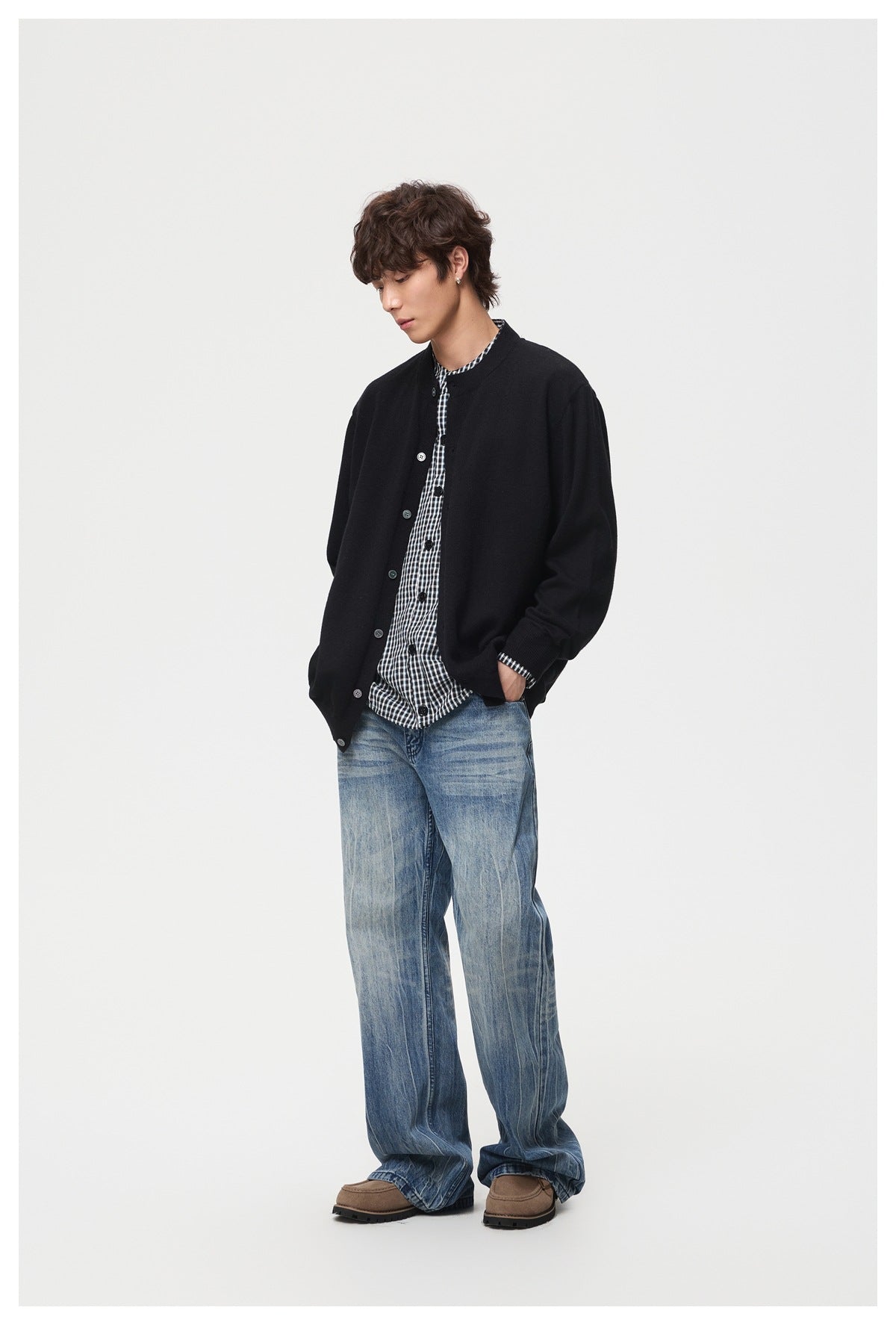 Model wearing a black button-front cardigan over a black-and-white checked shirt with loose blue jeans.