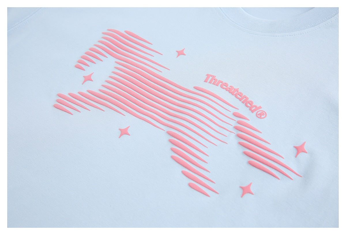 Close-up of a raised pink striped graphic, stars, and “Threatened®” lettering on a pale blue T-shirt.
