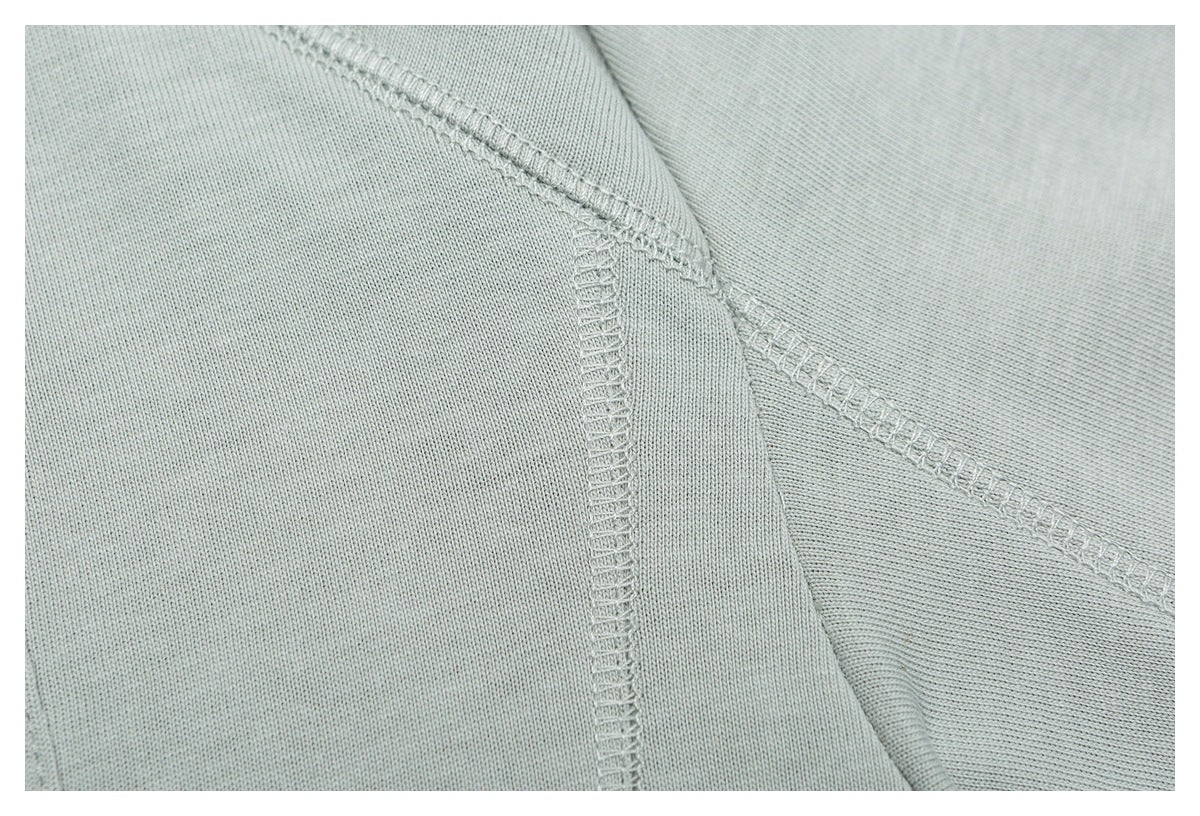 Close-up of overlocked seams on pale sage-gray knit fabric.