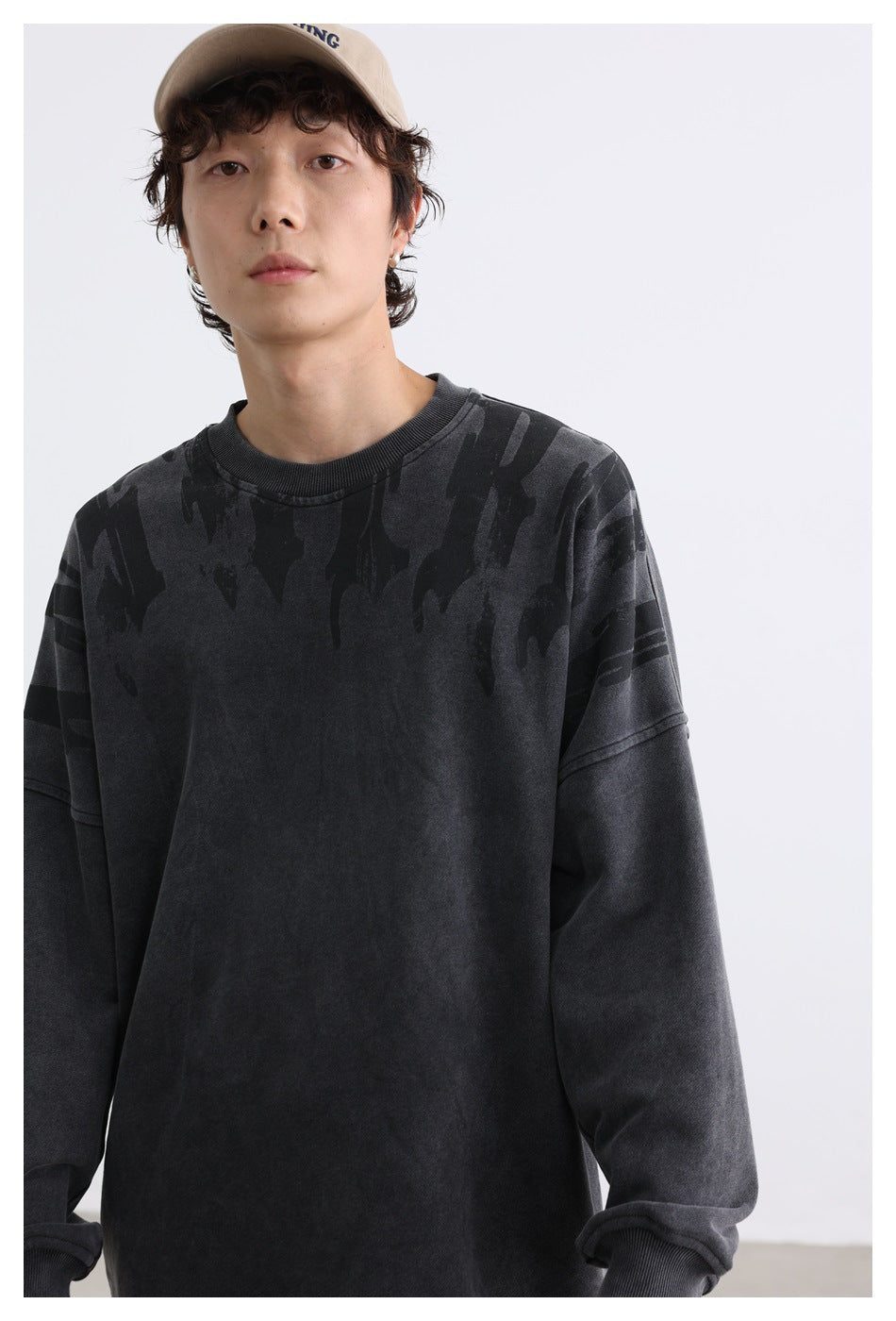 Close view of a charcoal crewneck sweatshirt with dark shoulder graphics, worn by a model.