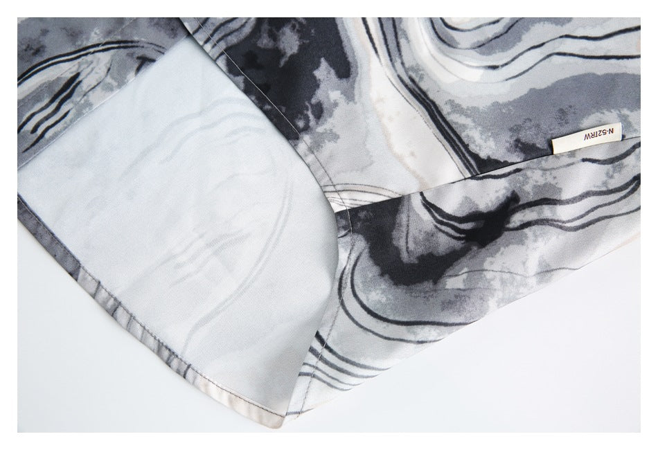Close-up of a gray, black, and off-white abstract-patterned garment hem with stitching and a small sewn label.