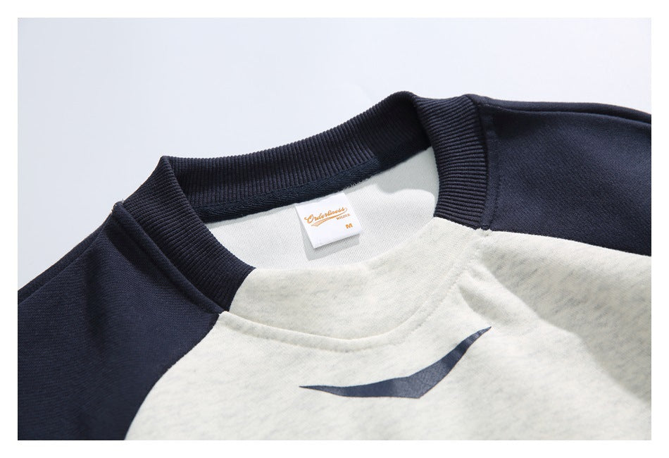 Close-up of a sweatshirt's navy ribbed crew neck, light gray body, and small printed chest graphic.