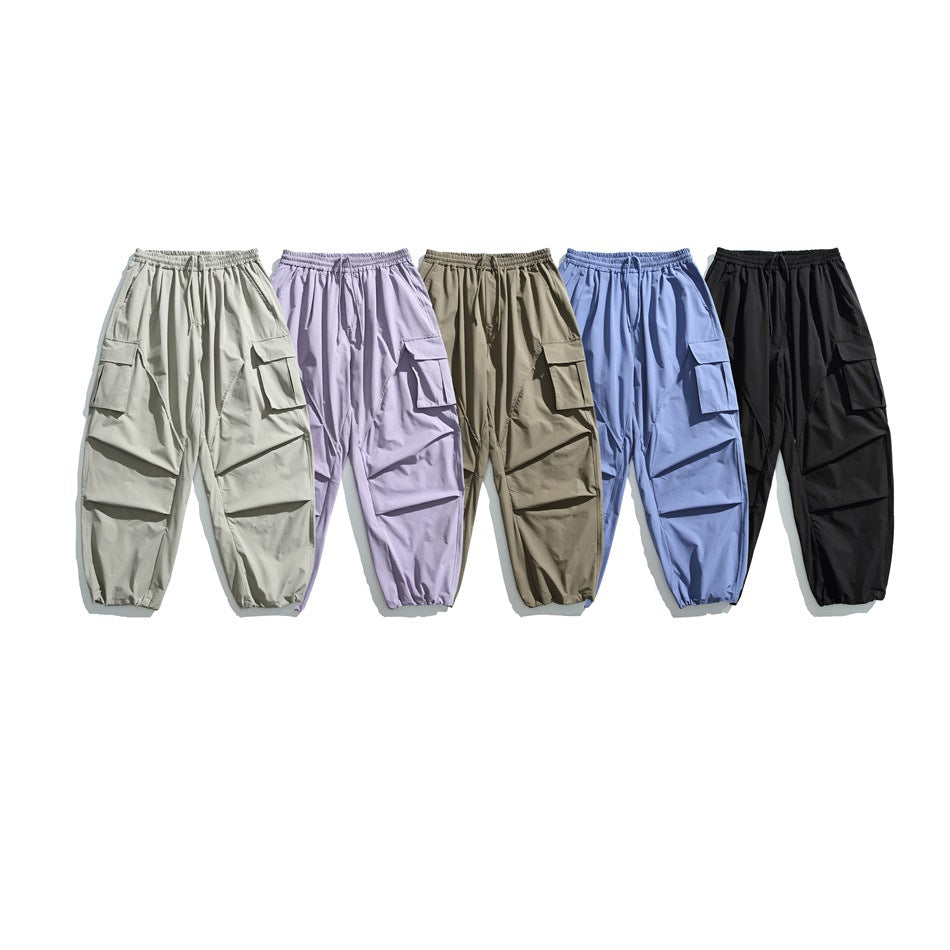 Five pairs of loose cargo pants with flap pockets in light gray, lavender, taupe, blue, and black.