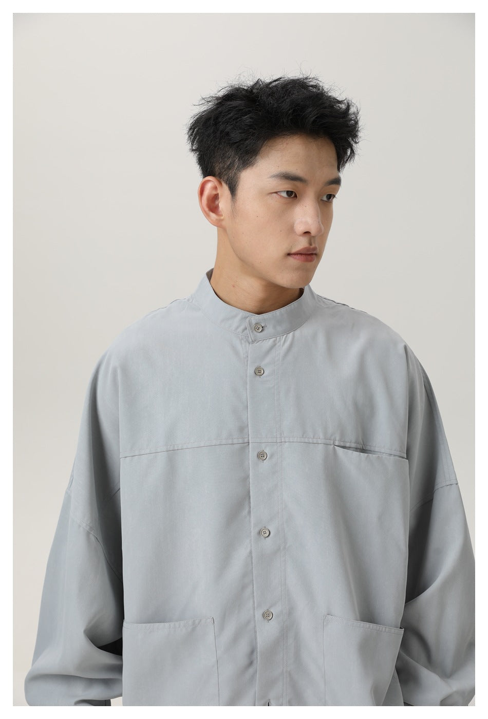 Model wearing a light gray button-front shirt with a stand collar, dropped shoulders, and two large front pockets.