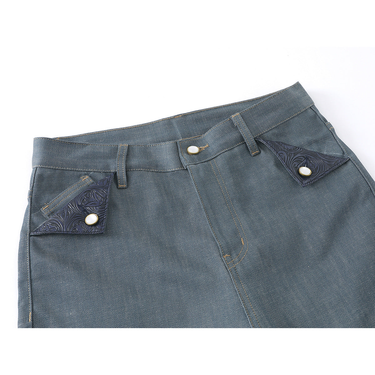 Close-up of blue-gray jeans showing the waistband, fly, and ornate dark pocket flaps with buttons.