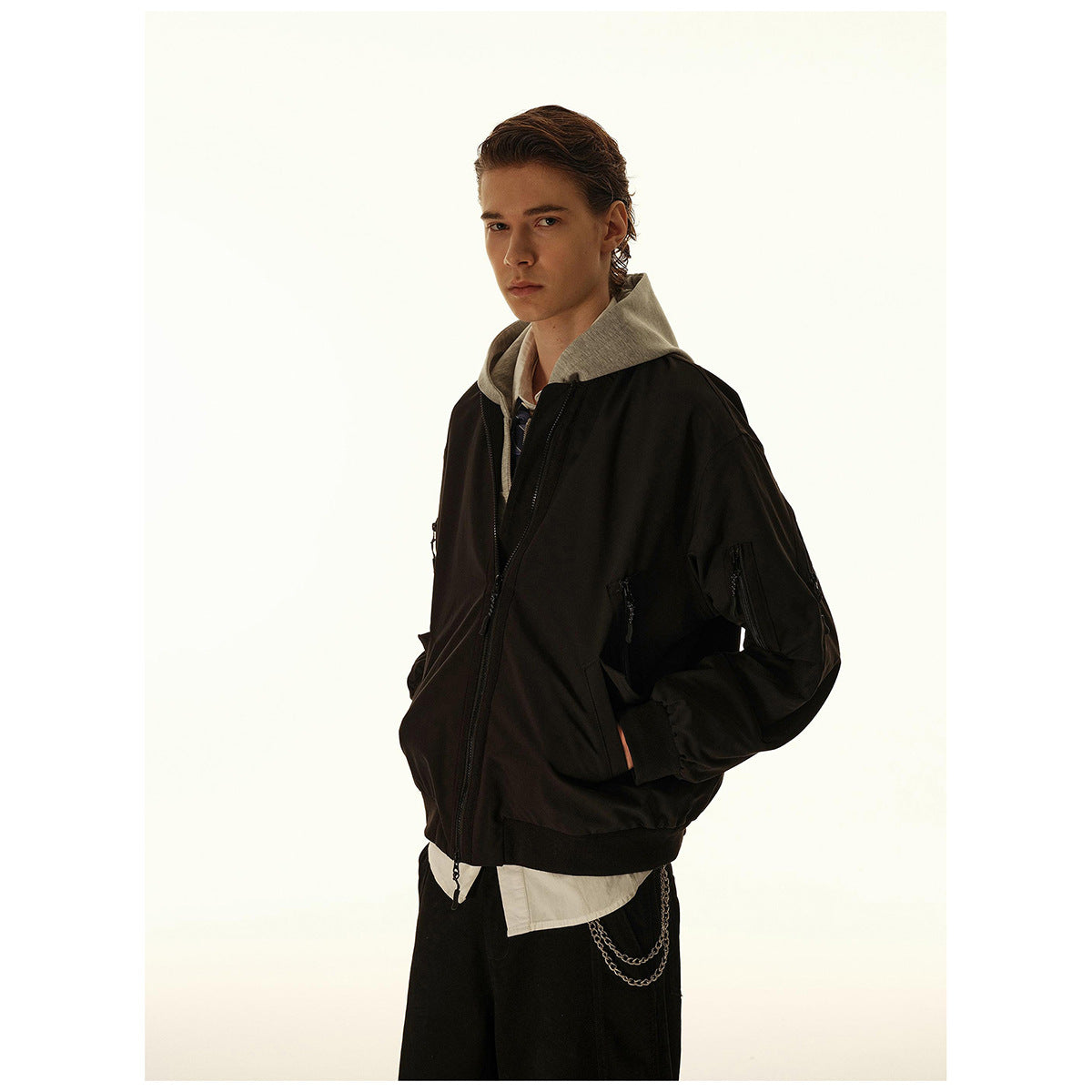 Man wearing a black zip-front bomber jacket over a gray hoodie, shown from an angled front view.