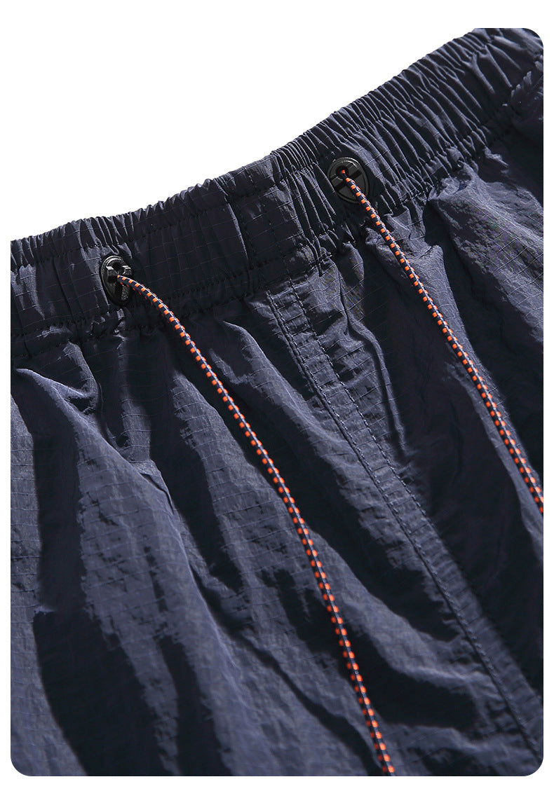 Close-up of dark shorts showing the elastic waistband, eyelets, and orange-and-black drawcords.