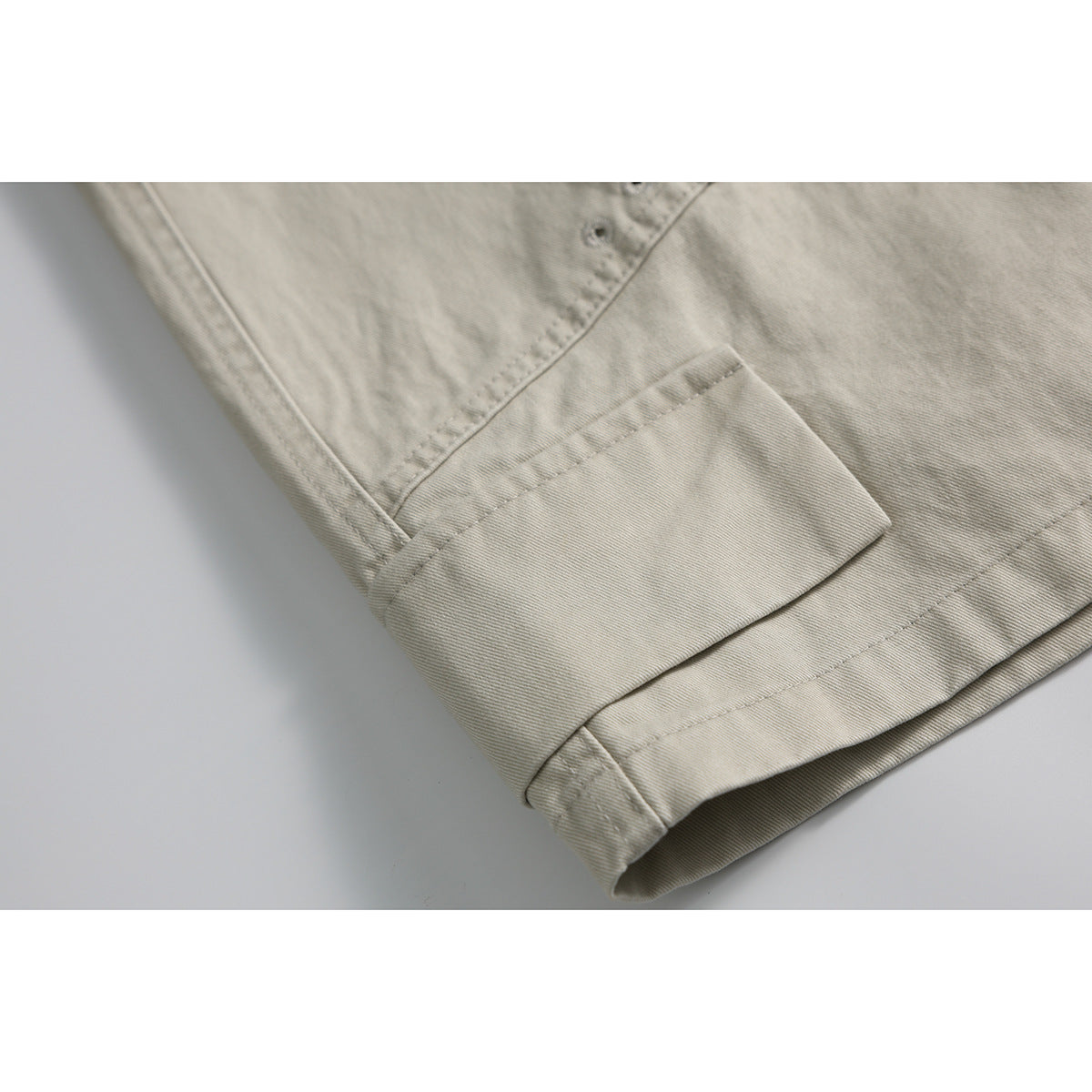 Close-up of light beige shorts showing a wide cuffed hem and visible stitching.