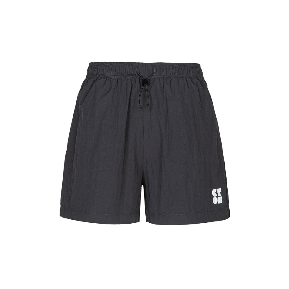 Black crinkled shorts with elastic waist, drawcord toggle and small white print on the lower left leg, front view