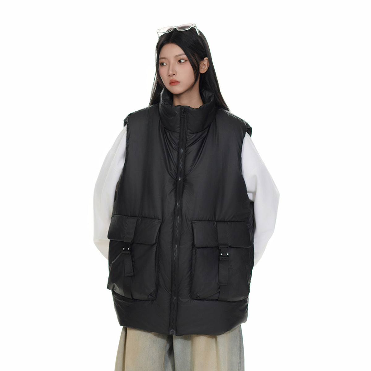 Model wearing a black padded high-collar vest with a front zip and large buckle-detail pockets over white sleeves.