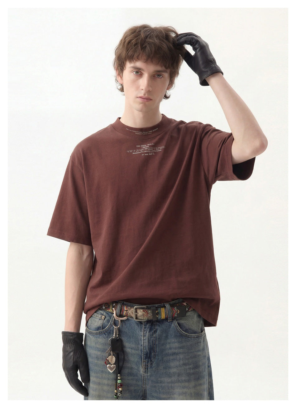 Model in a burgundy oversized T-shirt with small chest text, shown close-up with blue jeans, a patterned belt, and black