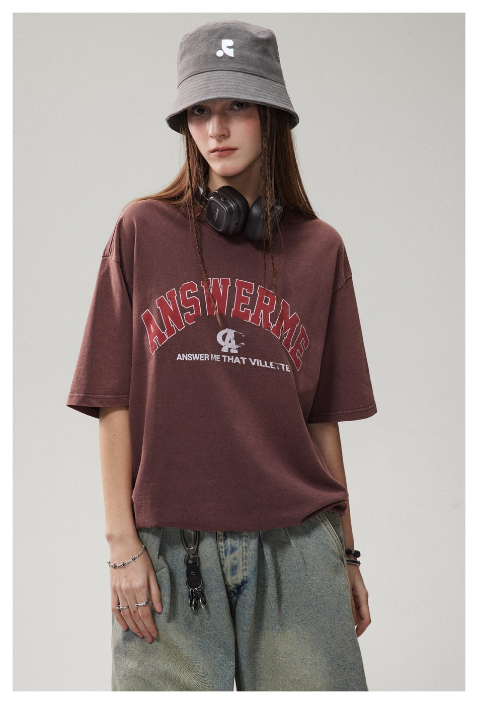 Front view of a model in a burgundy graphic T-shirt and gray bucket hat, with headphones around her neck.