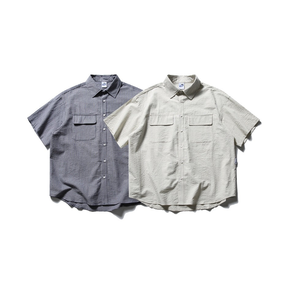 Two short-sleeve button-up shirts with flap chest pockets, one dark gray and one light gray, shown from the front.