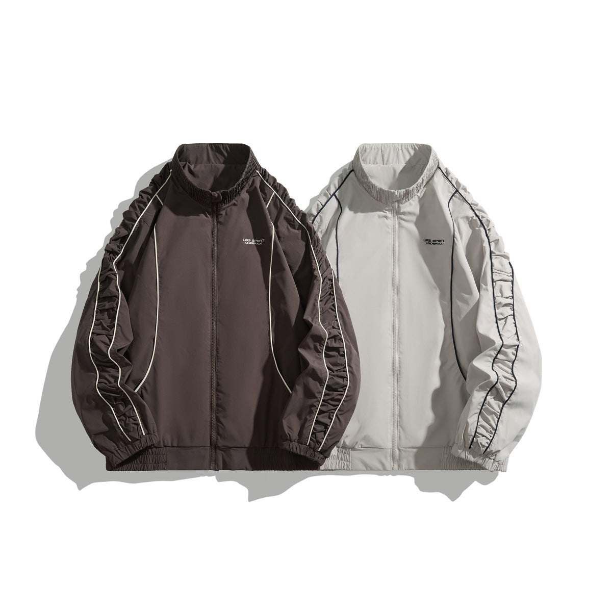 Two zip-up jackets shown from the front: dark brown with light piping and light gray with dark piping.