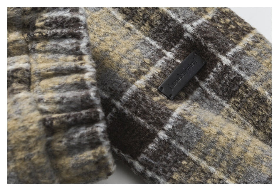 Close-up of a dark brand tab on brown, charcoal and tan plaid fabric beside a ribbed cuff.
