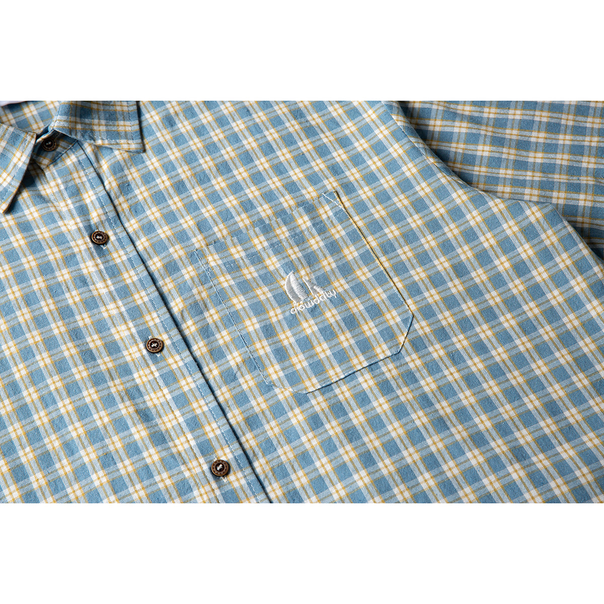 Close-up of a blue, white, and mustard plaid shirt showing its button placket, chest pocket, and small embroidery.
