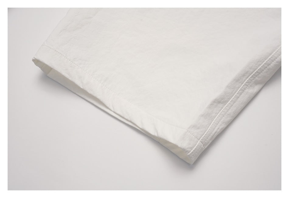 Close-up of the stitched hem on an off-white garment, laid flat.