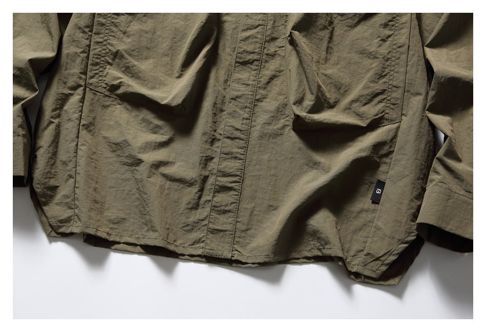 Close-up of the olive-brown shirt's lower front, showing its covered placket, large pockets, and small black tab.