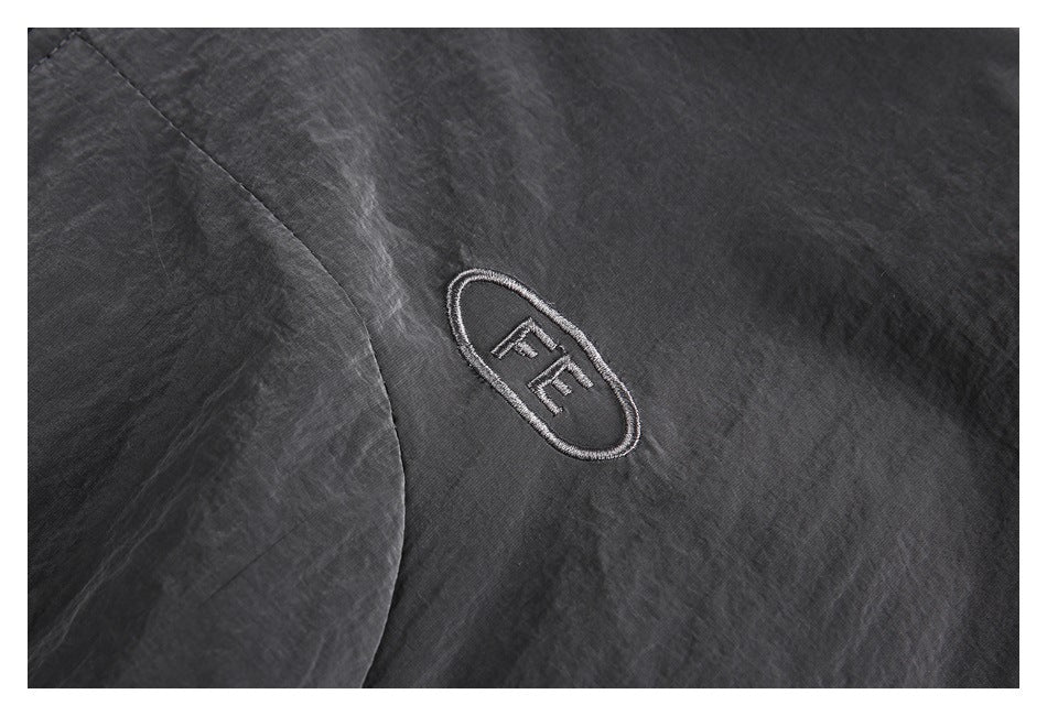 Close-up of an embroidered oval FE emblem on charcoal gray jacket fabric.