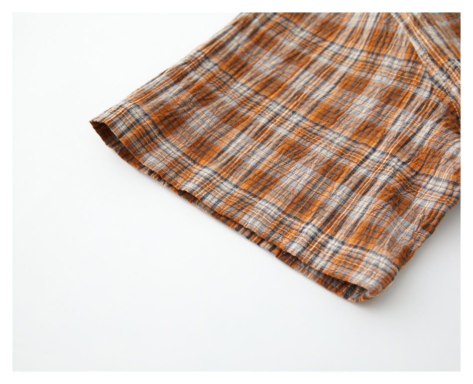 Close-up of the hem and edge of an orange, gray, and cream plaid garment.